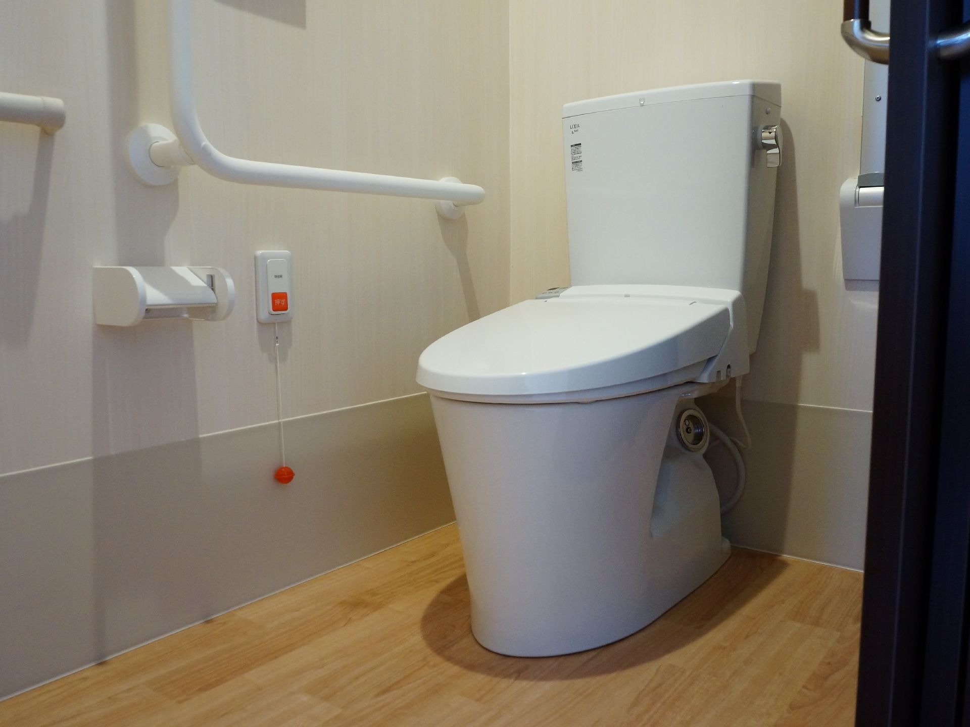 トイレには洋式便器が設置されている。壁側には転倒防止の手すりと緊急用に呼び出しボタンが付けられている。