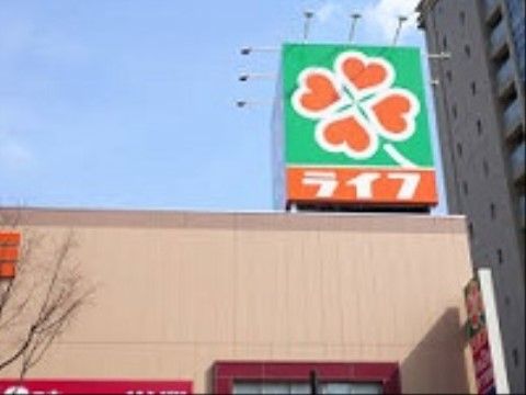 地域のスーパーマーケットの建物の外観で、外壁はベージュ基調になっている。屋上には看板が設けられ、店名が表示されている。