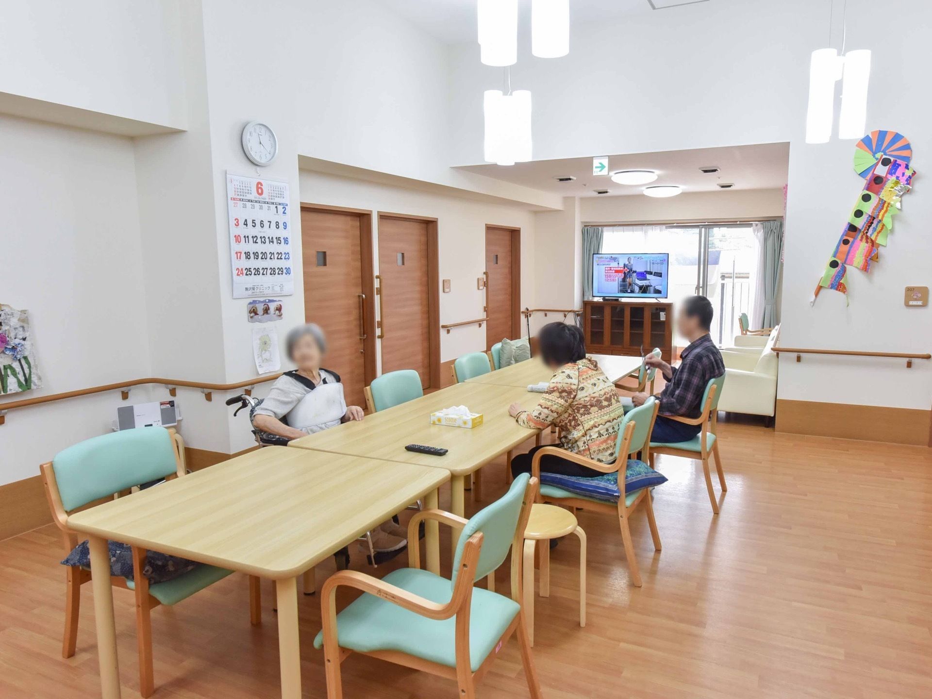 奥の突き当りにテレビが設置されている。その近くには白色のソファが２台置かれている。テレビは食卓からでも見やすい場所に位置している。