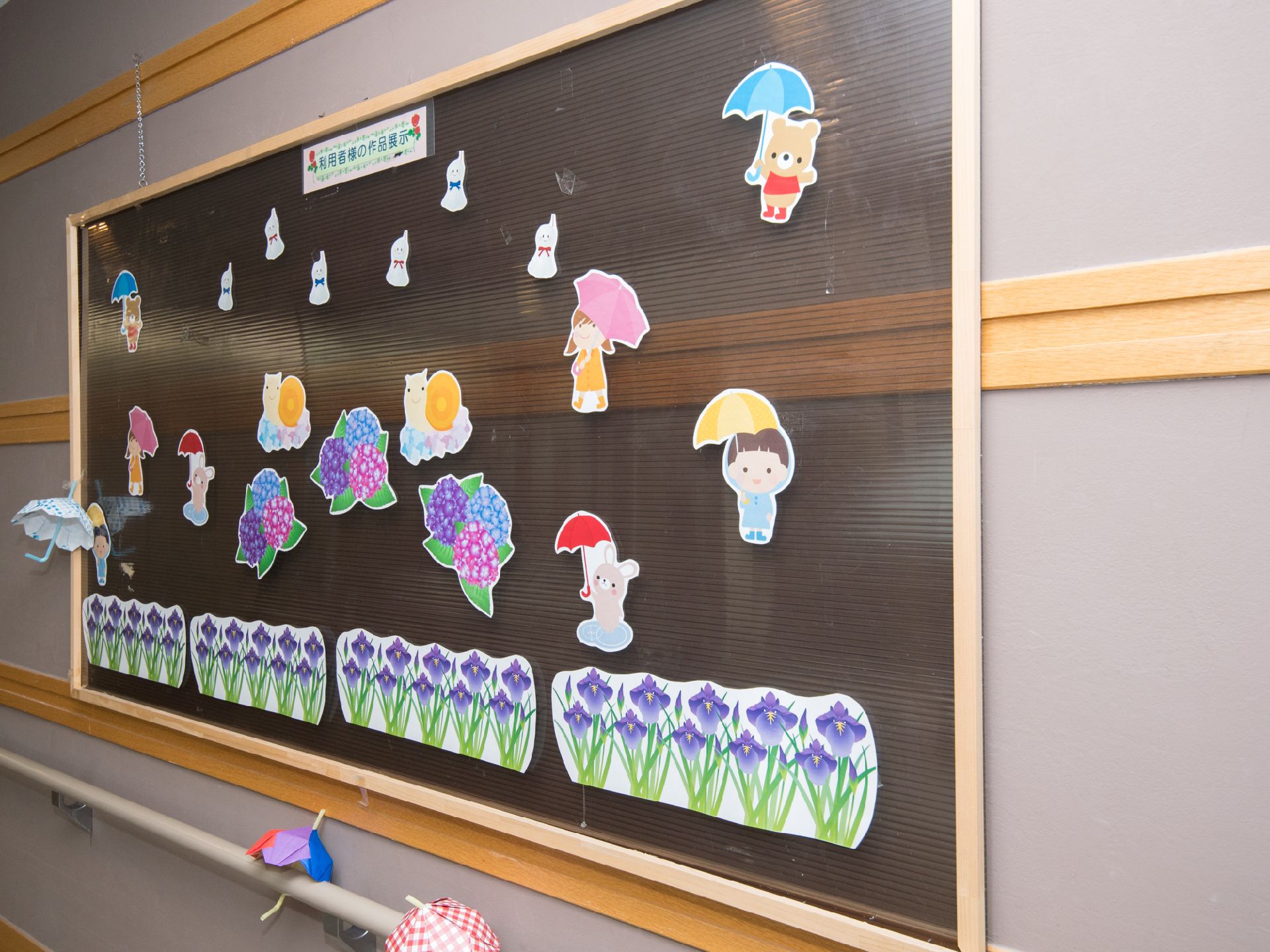 入居者の方の作品などを飾るスペース。工作の傘や傘をさしたクマ、子供、花、カタツムリなどが描かれている。