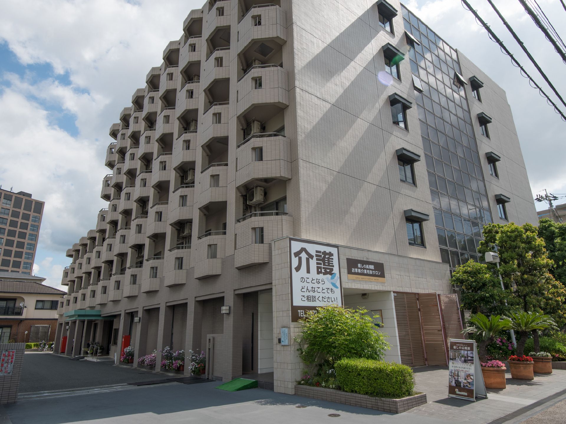 周囲に花や木が植えられた、六階建てのマンションのような建物