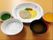白いおかゆとみそ汁、大きな白いお皿に盛られた主菜と緑色の副菜やオレンジ色のゼリーが並んでいる。彩りもよく飲み込みやすく工夫されている。