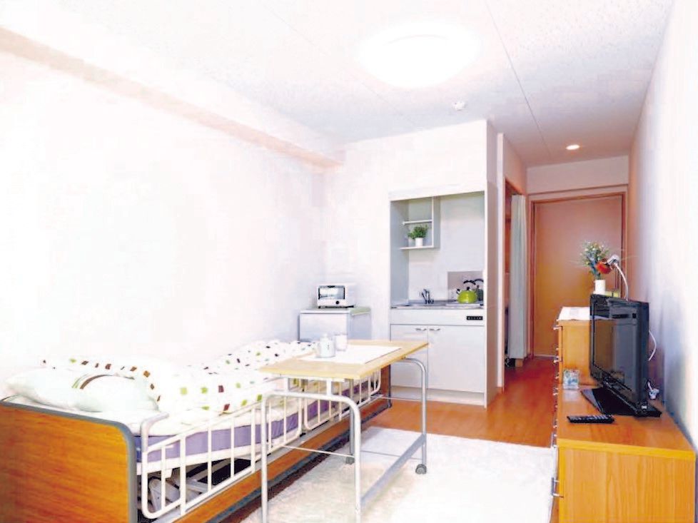 明るい部屋の入り口のすぐ脇にトイレなどがあり、居室部分にはミニキッチンがある。リクライニングベッドには、補助テーブルもついている。