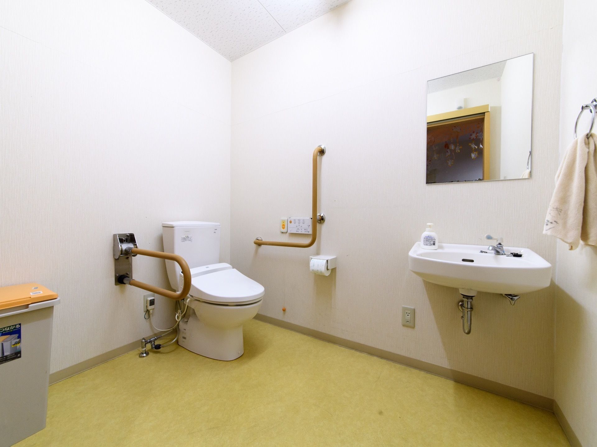 温水洗浄便座が備わったトイレスペース。手すりが備わっているので、立ち座りをしっかり補助してくれる。鏡付きの洗面台が付いている。