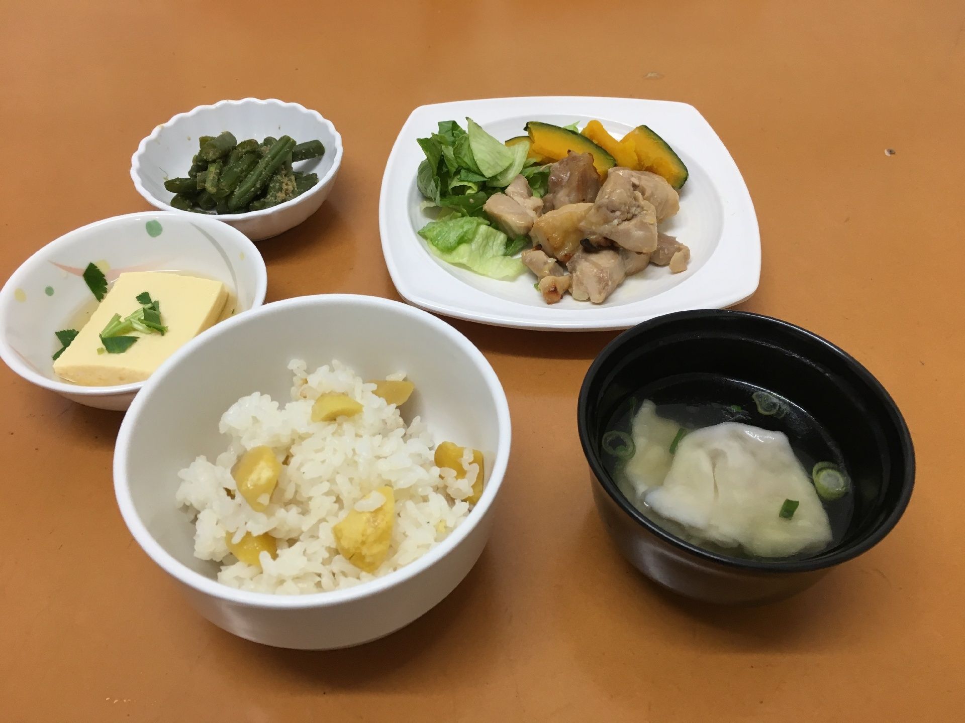 栗ご飯や水餃子、鶏肉の炒め物、いんげんの胡麻和え、湯豆腐が並べられている。メインディッシュにはレタスやかぼちゃが添えられている。