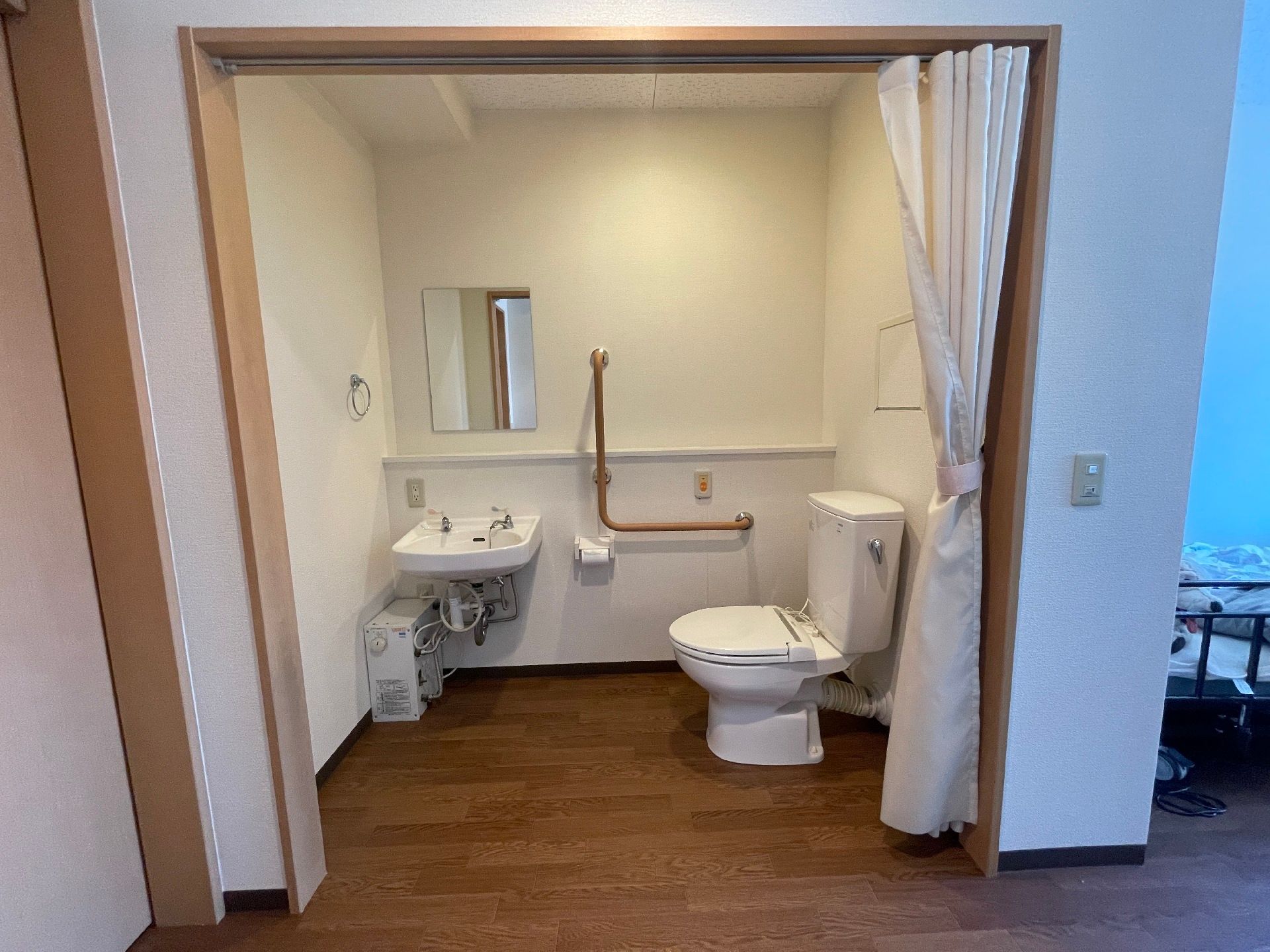エル字型の手すりやオレンジの呼び出しボタンが付いたトイレには手洗い場があり、カーテンが付いている。