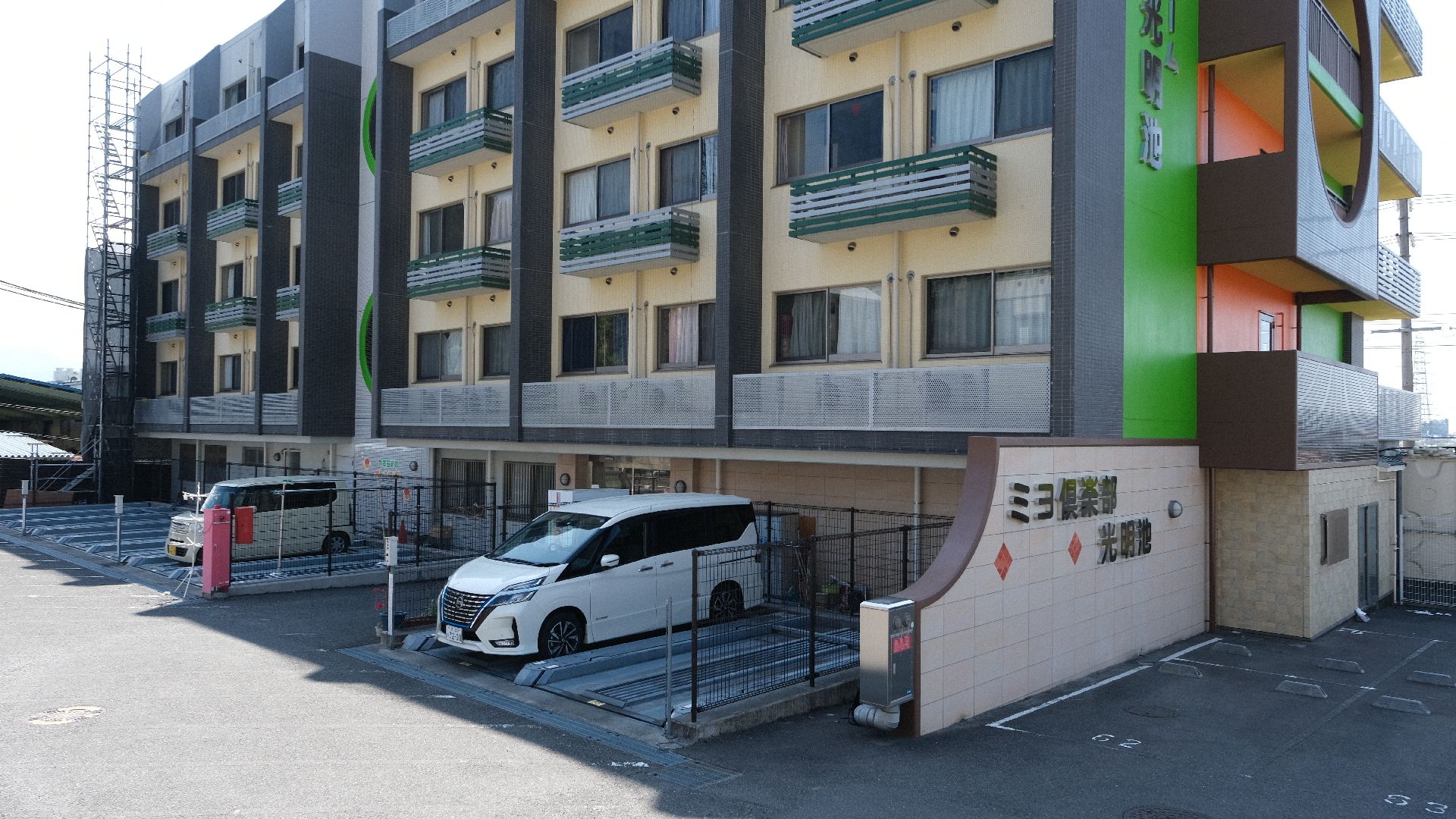 ベージュを基調とした建物の前には駐車場もあり、車が数台止められている。建物の裏側の外壁はカラフル。