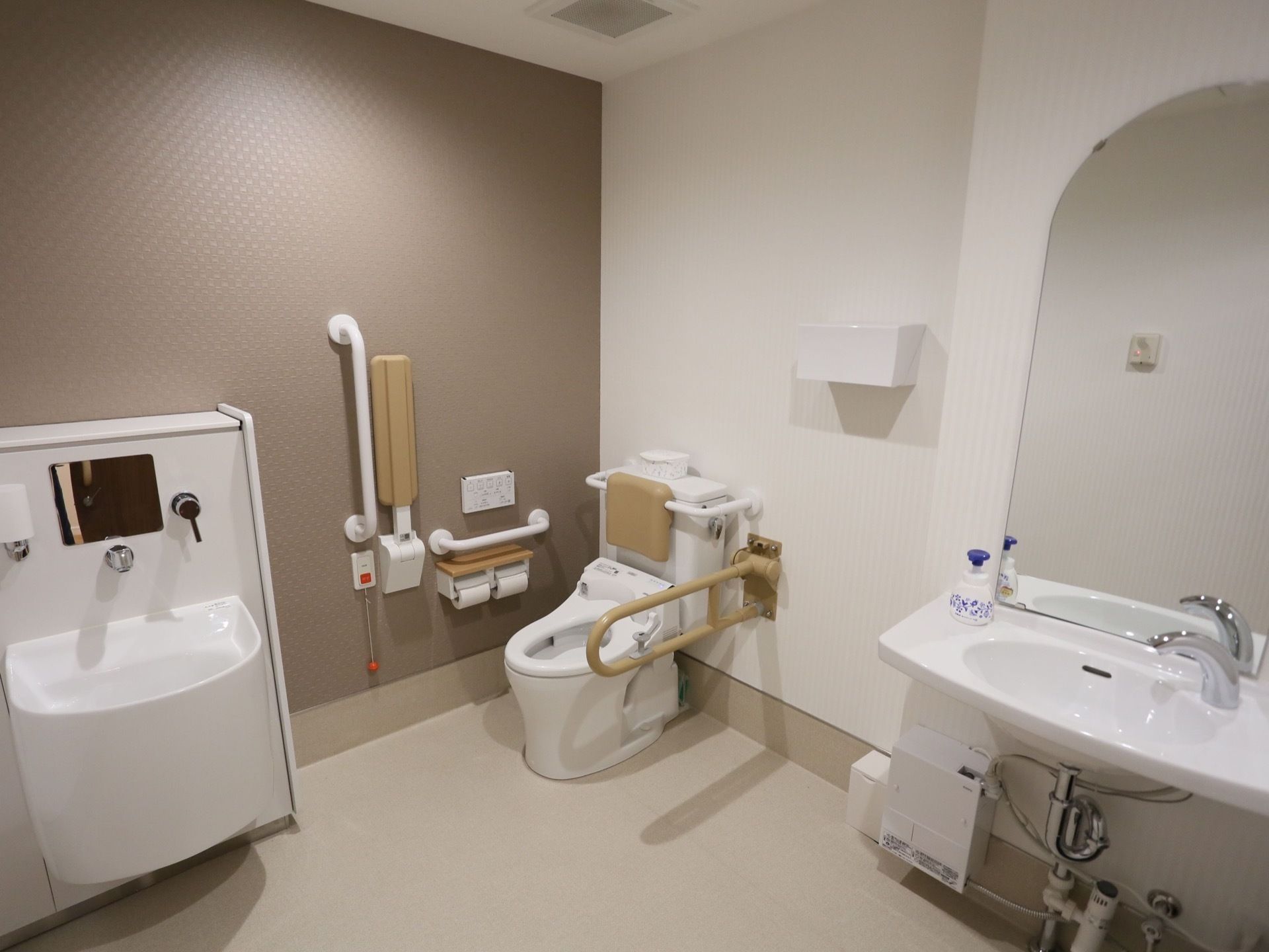 トイレは洋式で洗面台もある。白くしっかりと造りの手すりが取り付けられている。便器の周囲にはスペースが取られている。