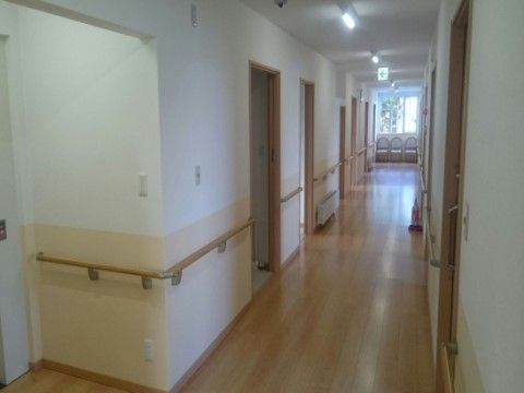廊下の突き当たりには窓があり、窓の前に椅子が並べられている。居室の扉が並んでおり、壁に手すりが取り付けられている。