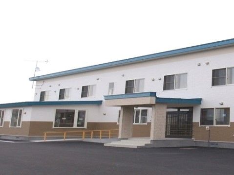白い外壁が爽やかな２階建ての建物である。玄関前は広々としており、スロープが設置されているので車椅子をご利用の方も楽に出入りできる。