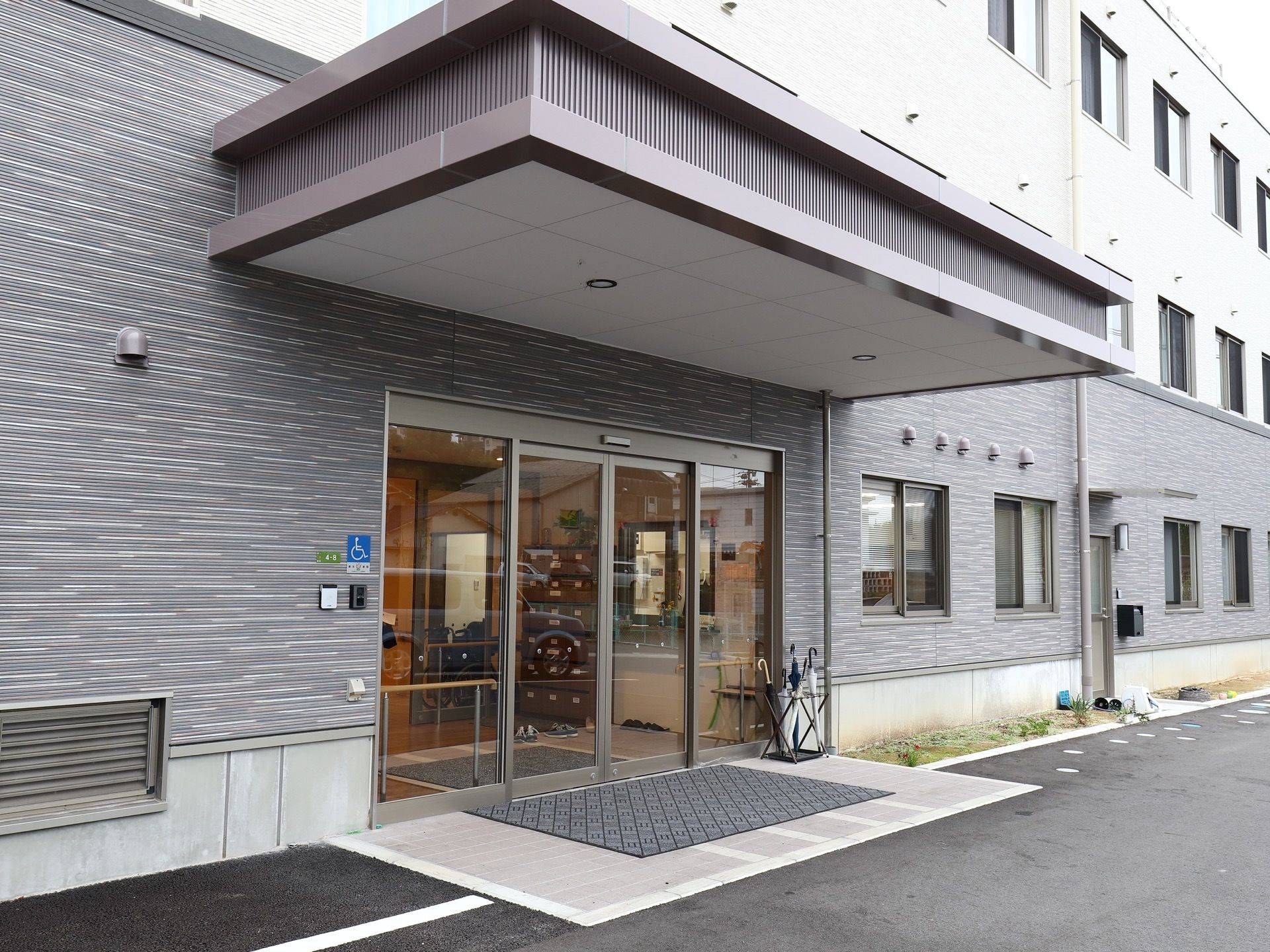 ガラス扉の自動ドアが使われた玄関。バリアフリー設計で、玄関マットが敷かれている。扉の内側には大きな下駄箱が設置されている。