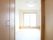 出入口から居室の中を見た様子である。手前の右手にはトイレの個室の扉があり、左手には収納、部屋の一番奥は窓である。