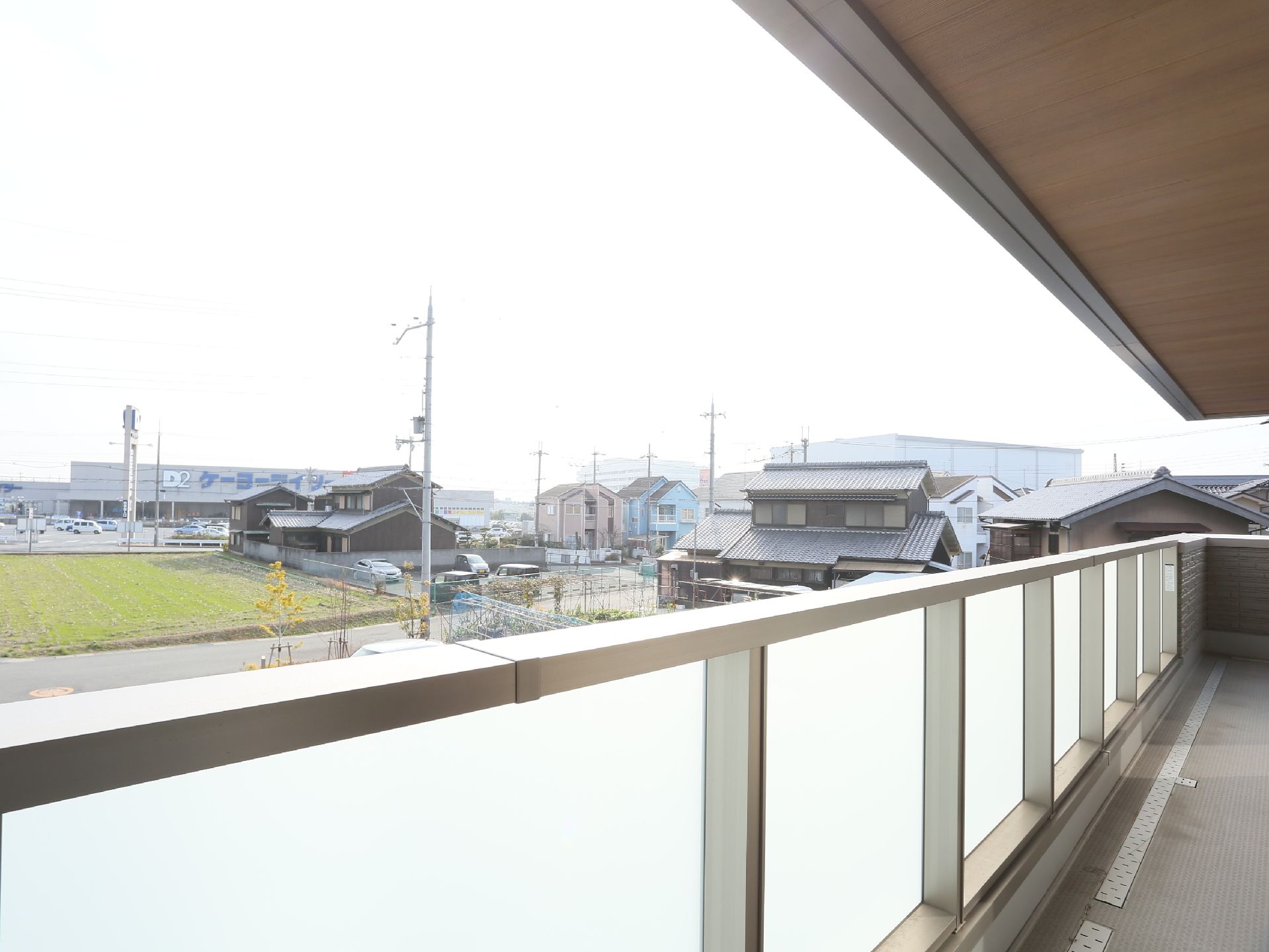 居住階に広いバルコニーが設けられており、目隠しパネルがついた手すりが設置されている。外には、畑や民家がある。