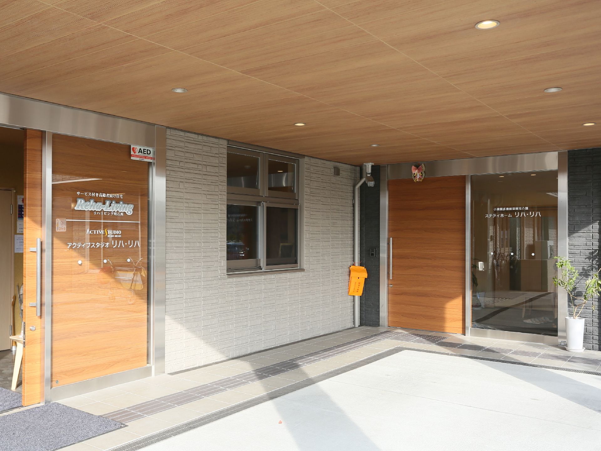 大きな屋根が設置された広いエントランスである。２箇所ある出入口の扉には、引き戸が採用されている。点字ブロックが設けられている。