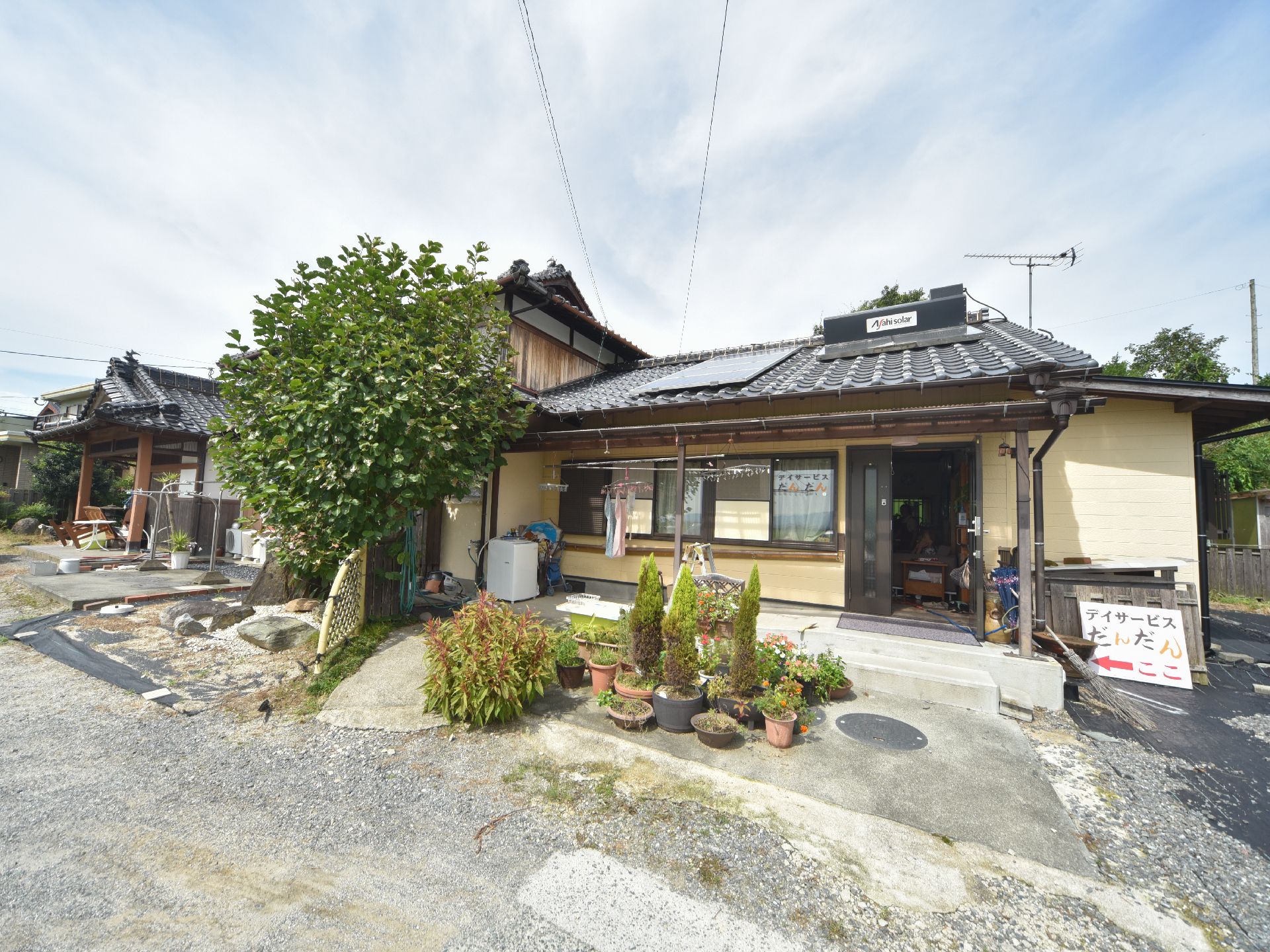 施設の建物の屋根は瓦ぶきで、ソーラーパネルが設置されている。建物前の地面は砂利敷きで、大きな石や植物などがある。