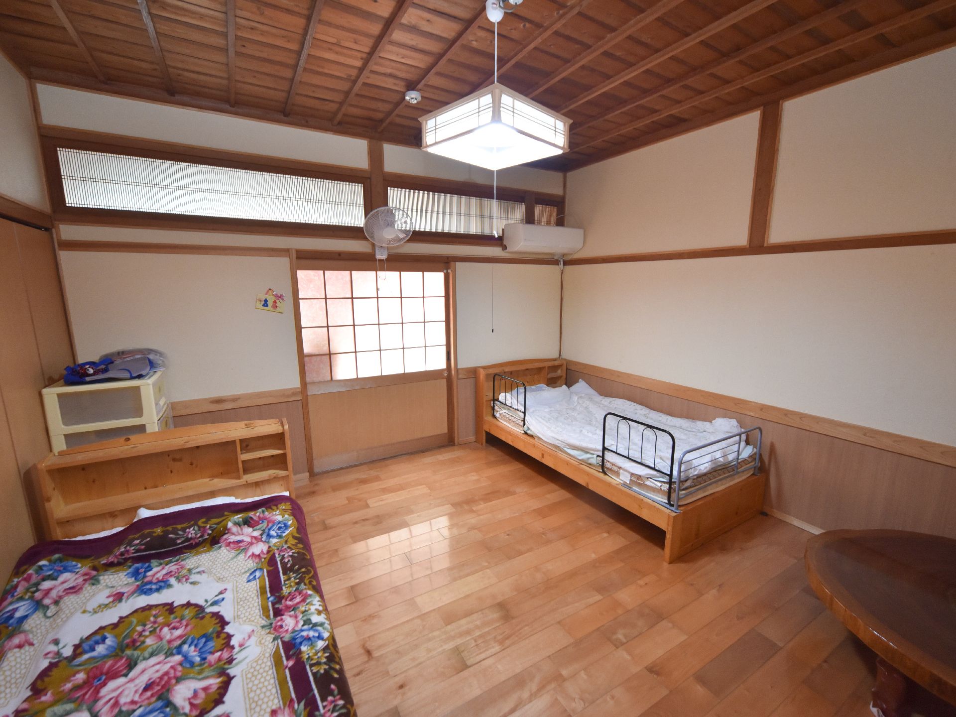 居室の床は艶のあるフローリングである。天井は高く、扉の上には欄間が設けられている。右側にエアコンが1台ある。