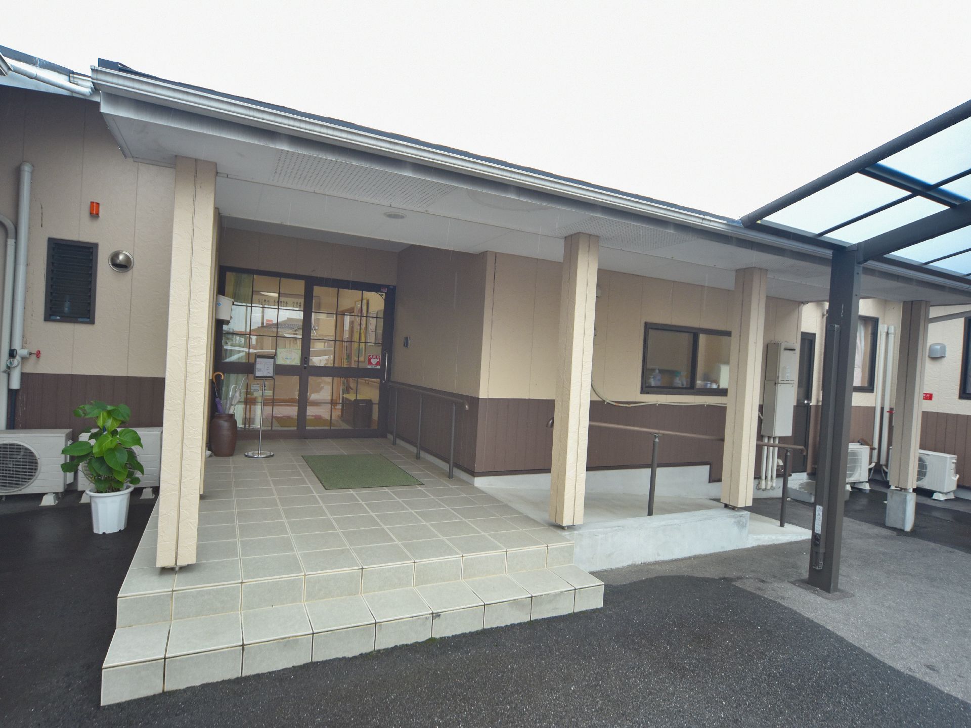 施設の玄関は黒いフレームのガラス張りで、中の様子が見えるようになっている。上部には大きな屋根が設置されている。