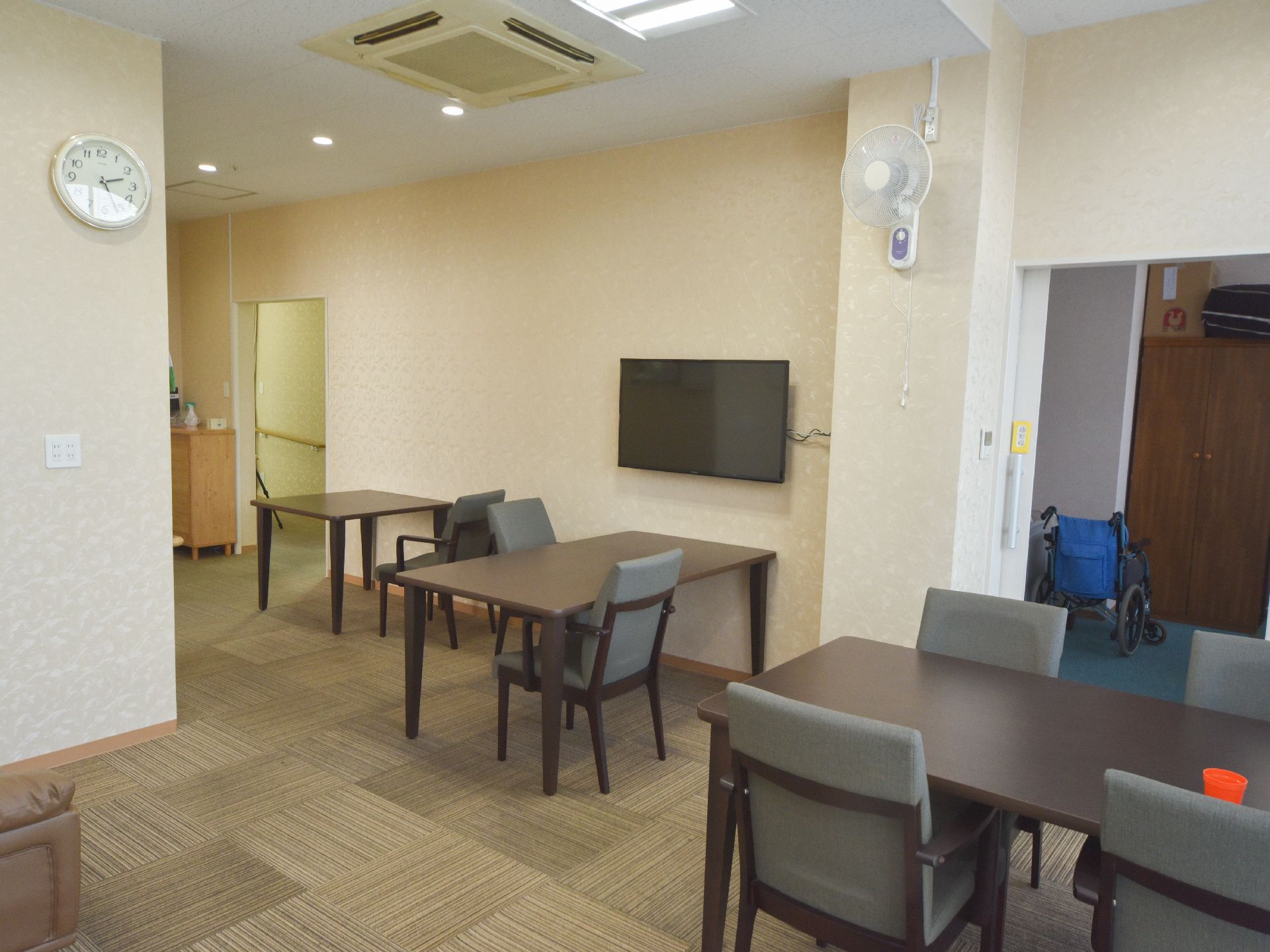 リビングダイニングは広い空間が確保されており、ダイニングテーブルが設置されている。薄型テレビや壁掛け扇風機、時計が備え付けられている。