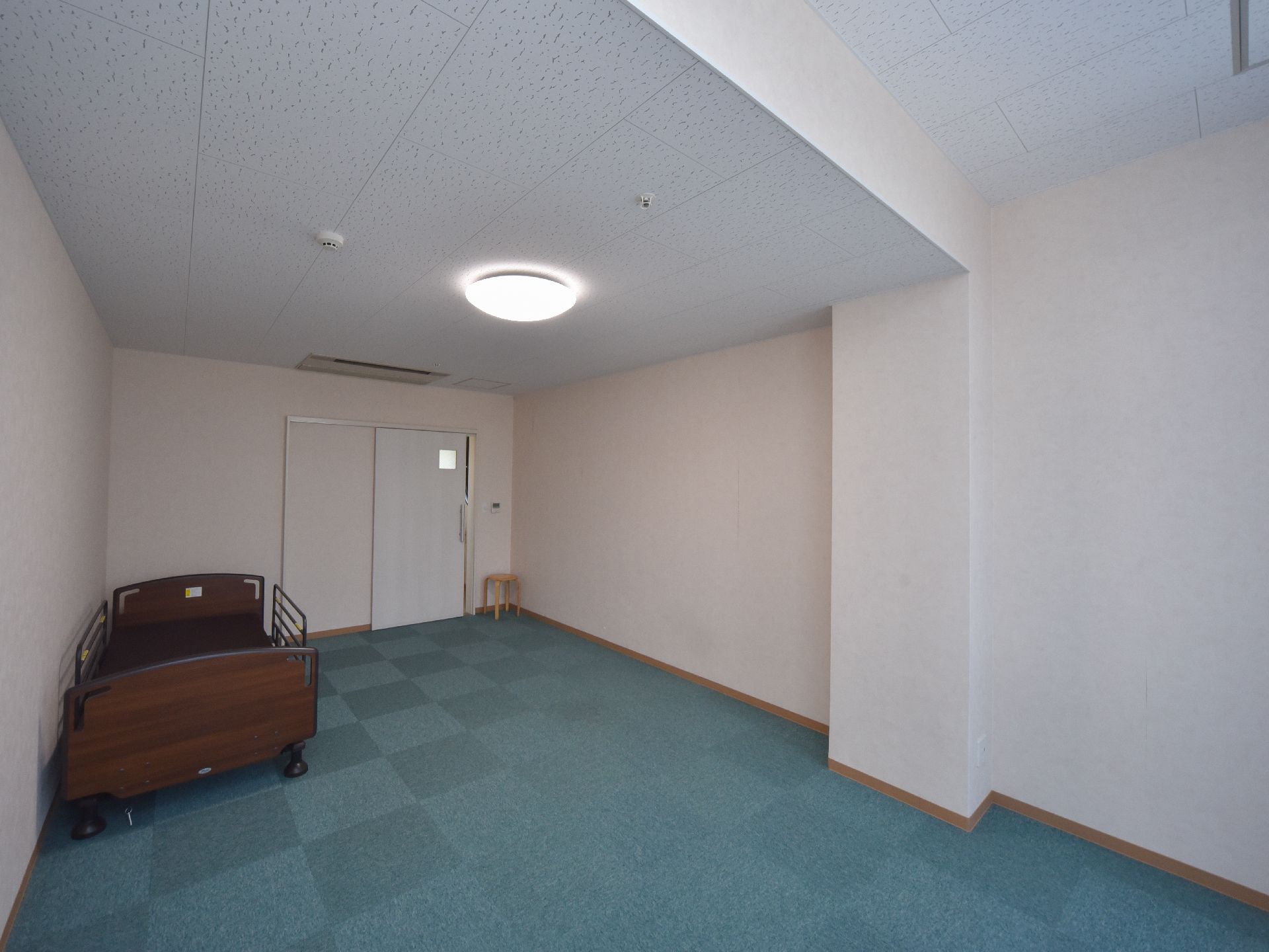 広々とした居室には介護ベッドや丸椅子が配置されている。ドアは高齢者でも開閉が楽なスライドドアになっている。
