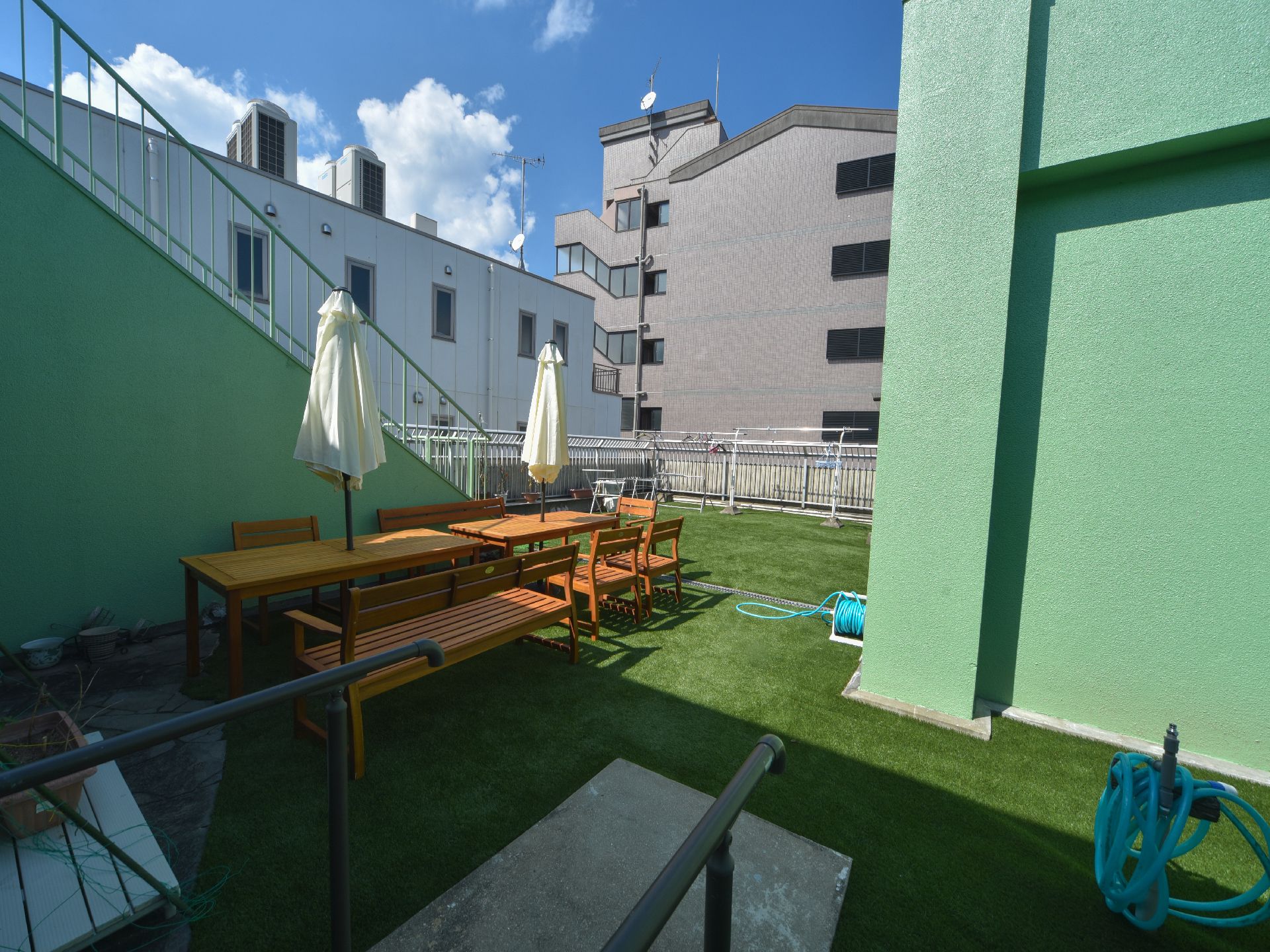 芝が敷かれた屋上には、白いパラソル付きのガーデンテーブルとベンチが置かれており、物干し台や手すり付きのスロープが設置されている。