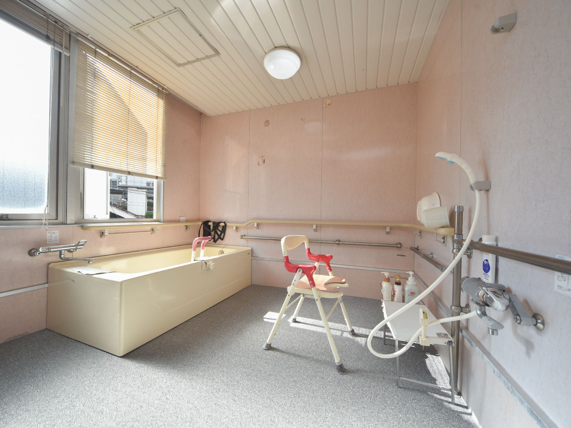 浴室には背の高い介護用風呂椅子や湯おけ、シャンプーなどが完備されている。複数の手すりが壁に備え付けられている。