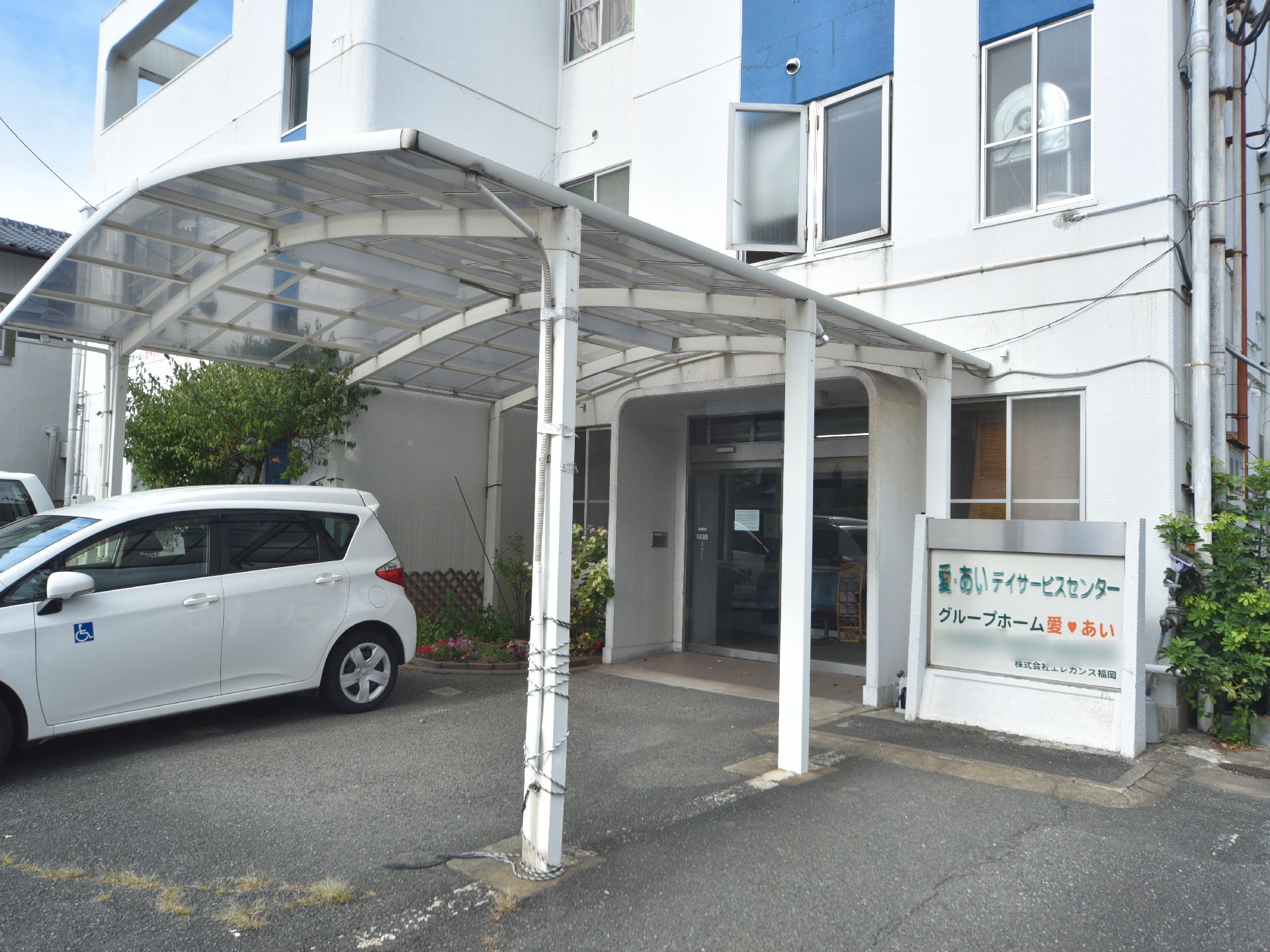 屋根付きのエントランスである。車を駐車することも可能。施設の名と電話番号が記された大きな看板が設置されている。