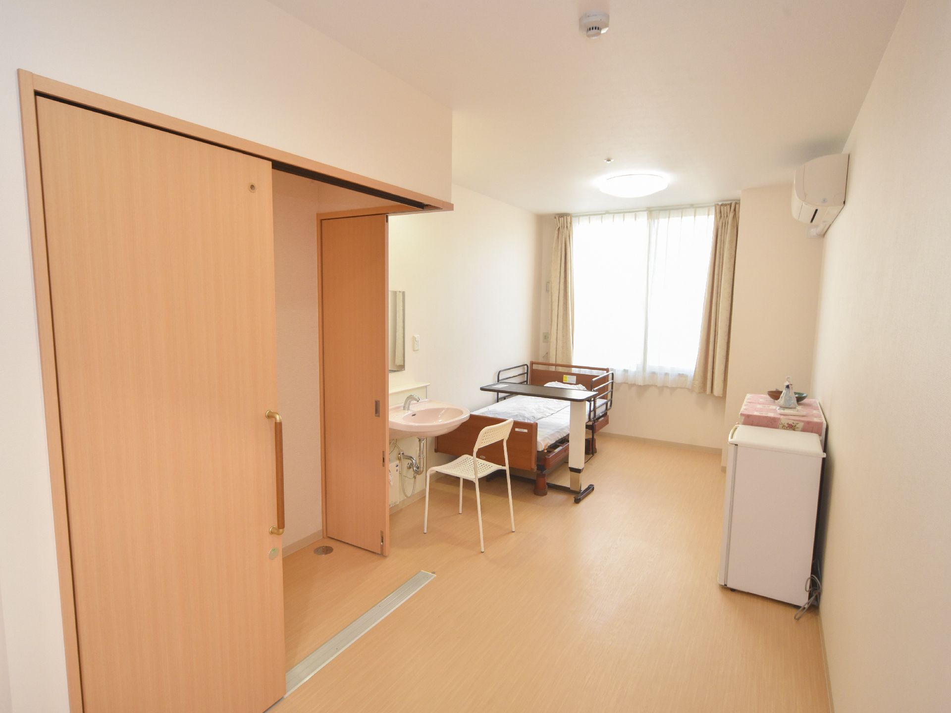 居室の床はフラットなフローリングで、左側のドア部分にのみレールが設置されている。壁際に冷蔵庫が置かれている。