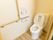 清潔感のある白壁とフローリングのトイレ内の様子。壁にはL字型の掴みやすい手すりとナースコールが設置されている。