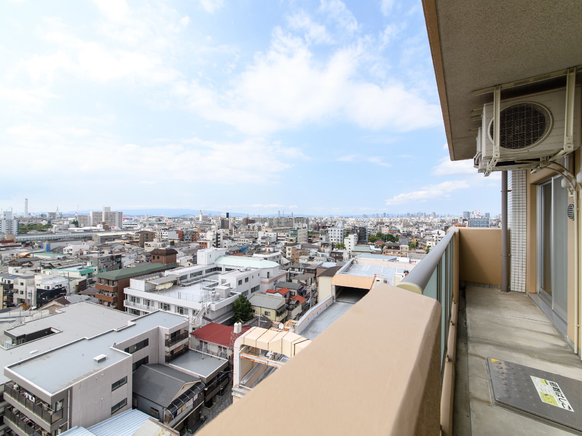 雲は多少あるが青空がベランダから見える。施設の周辺には、アパートなどが多く立ち並び、その間に古くからある一般住宅が所々残っている。