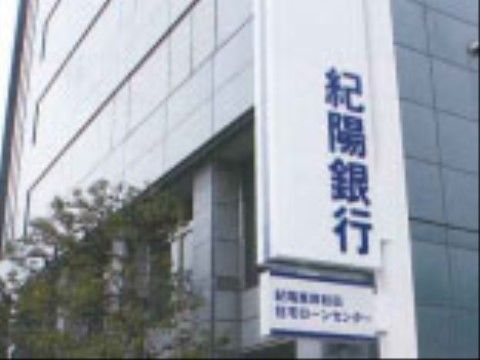 グレーの大きな建物に、紀陽銀行の名前が入った看板が設置されている。建物の前には、大き目の木が植えられている。