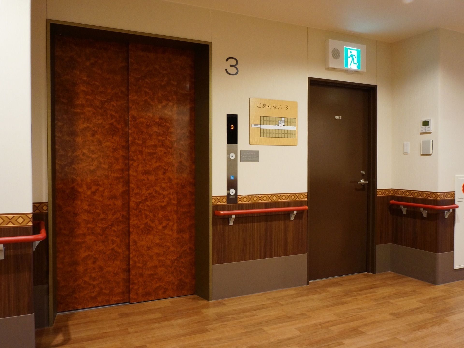 エレベーター前の床はフローリングで、通路と段差なく繋がっている。壁には操作パネルとフロアの案内図を掲示している。