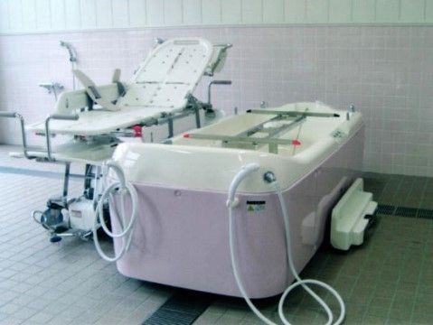 床と壁がタイル張りの明るく広い浴室。横になったままで入浴ができる介助浴槽と、ストレッチャーが置かれている。
