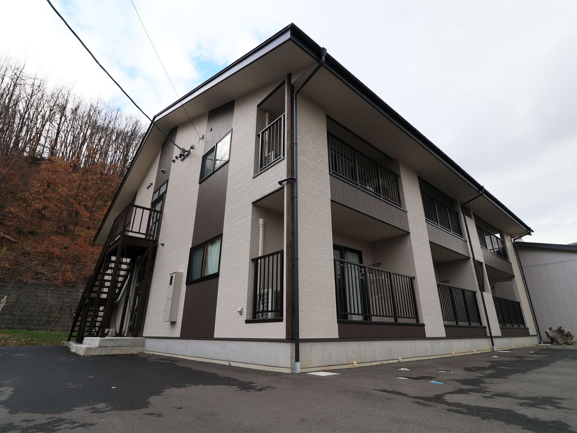 ベージュとブラウンのツートーンカラーの二階建ての建物がある。ベランダがあり、外つけの非常階段が設置されている。