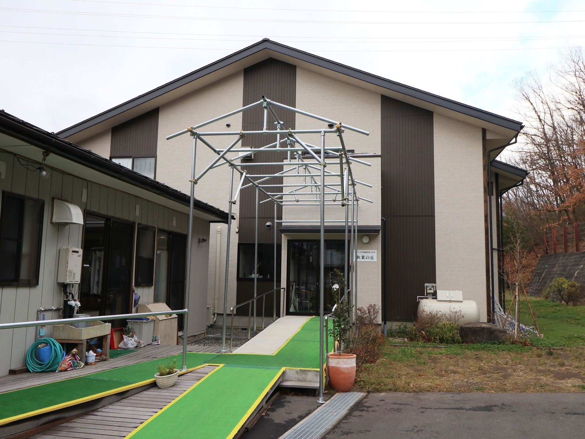 二階建てと平屋造りが合体した建物がある。玄関までは長いスロープと手すりが設置されている。周囲は草木が生い茂っていて自然豊かな環境である。