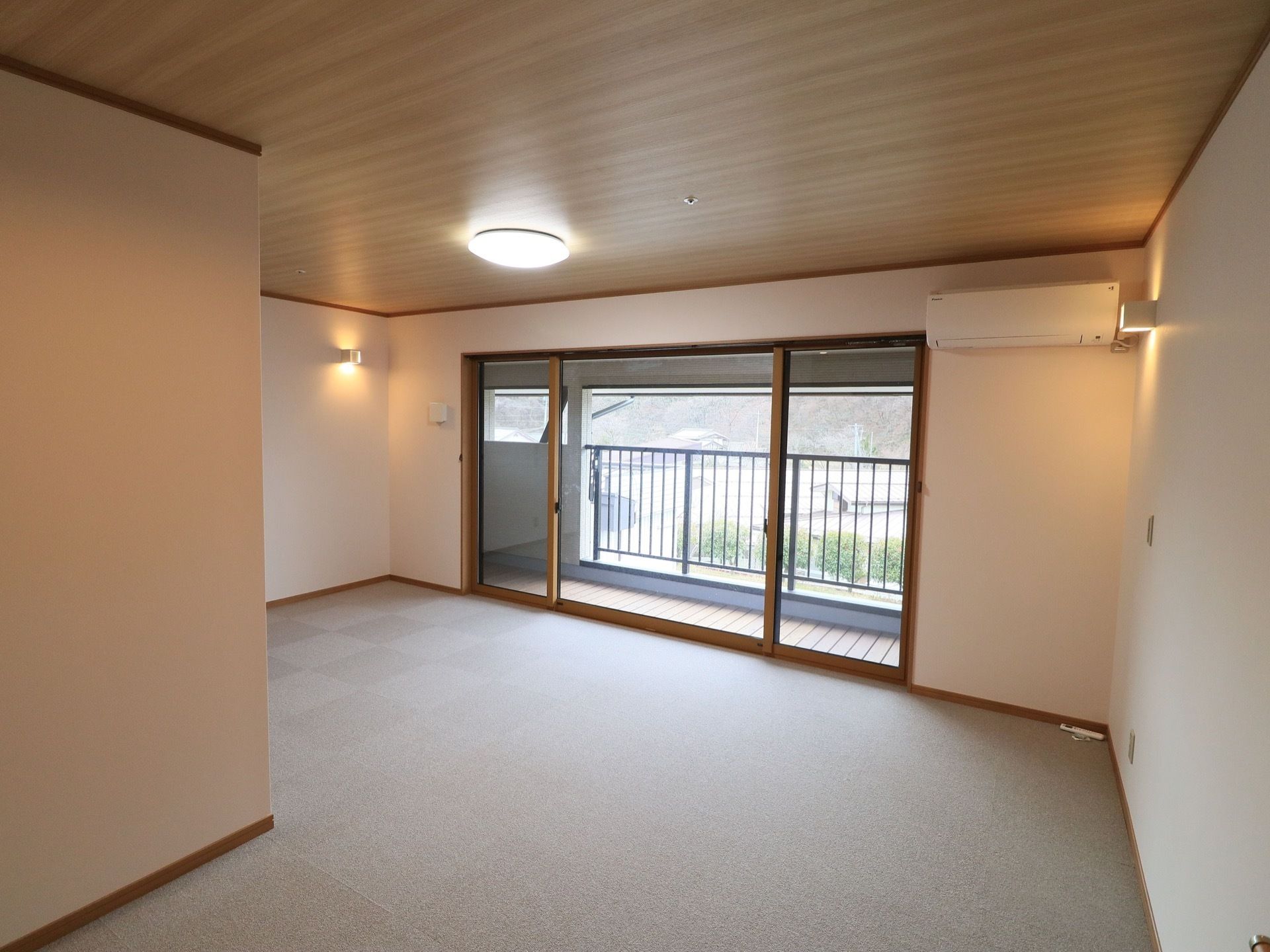 大きな窓のある入居者様の居室。床は絨毯敷きになっており、天井は木目調になっている。天井と壁には照明が複数ついている。