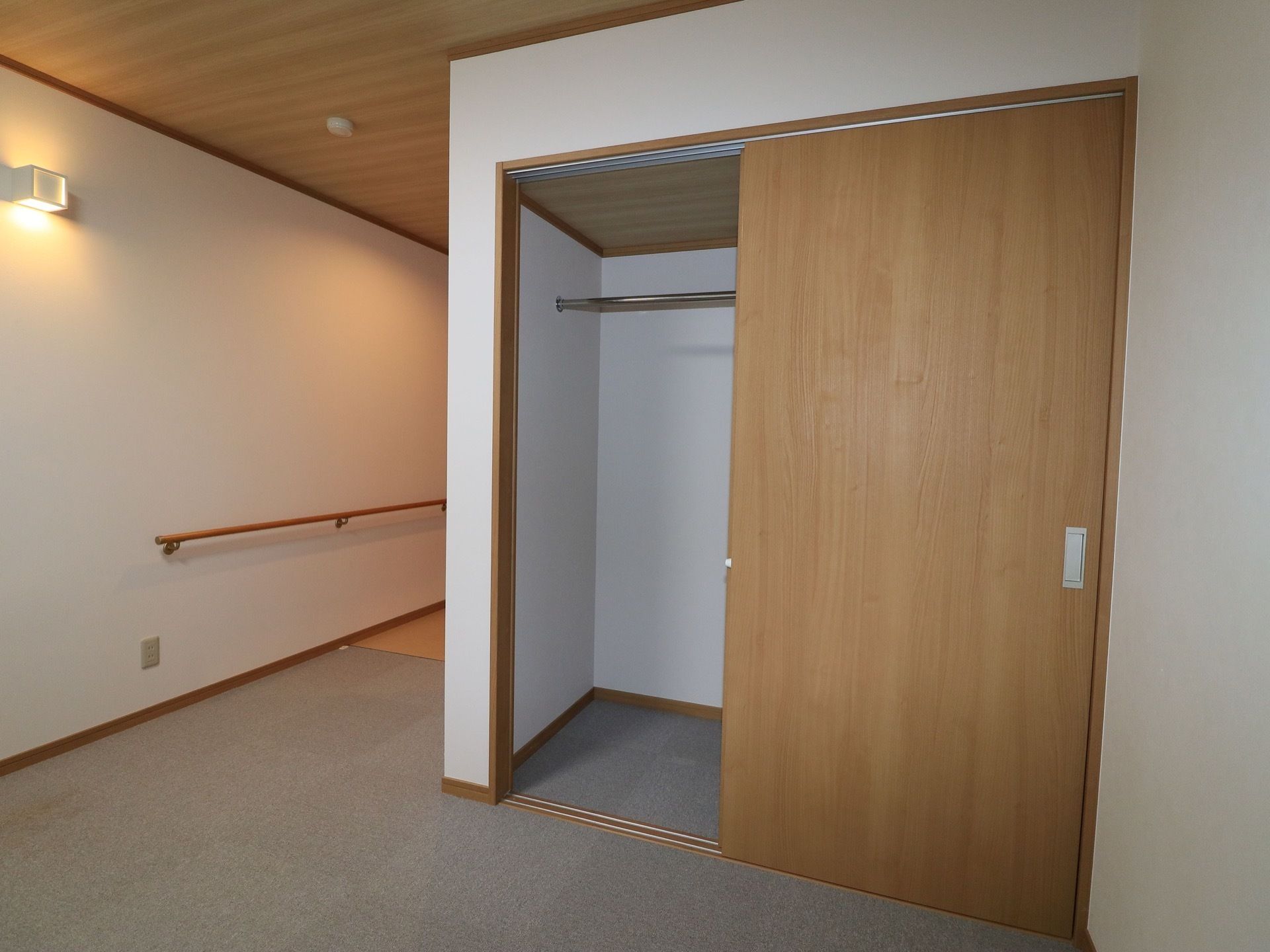入居者様の居室にあるクローゼット。木目調のスライド式の扉がついている。居室の壁には間接照明と手すりが設置されている。