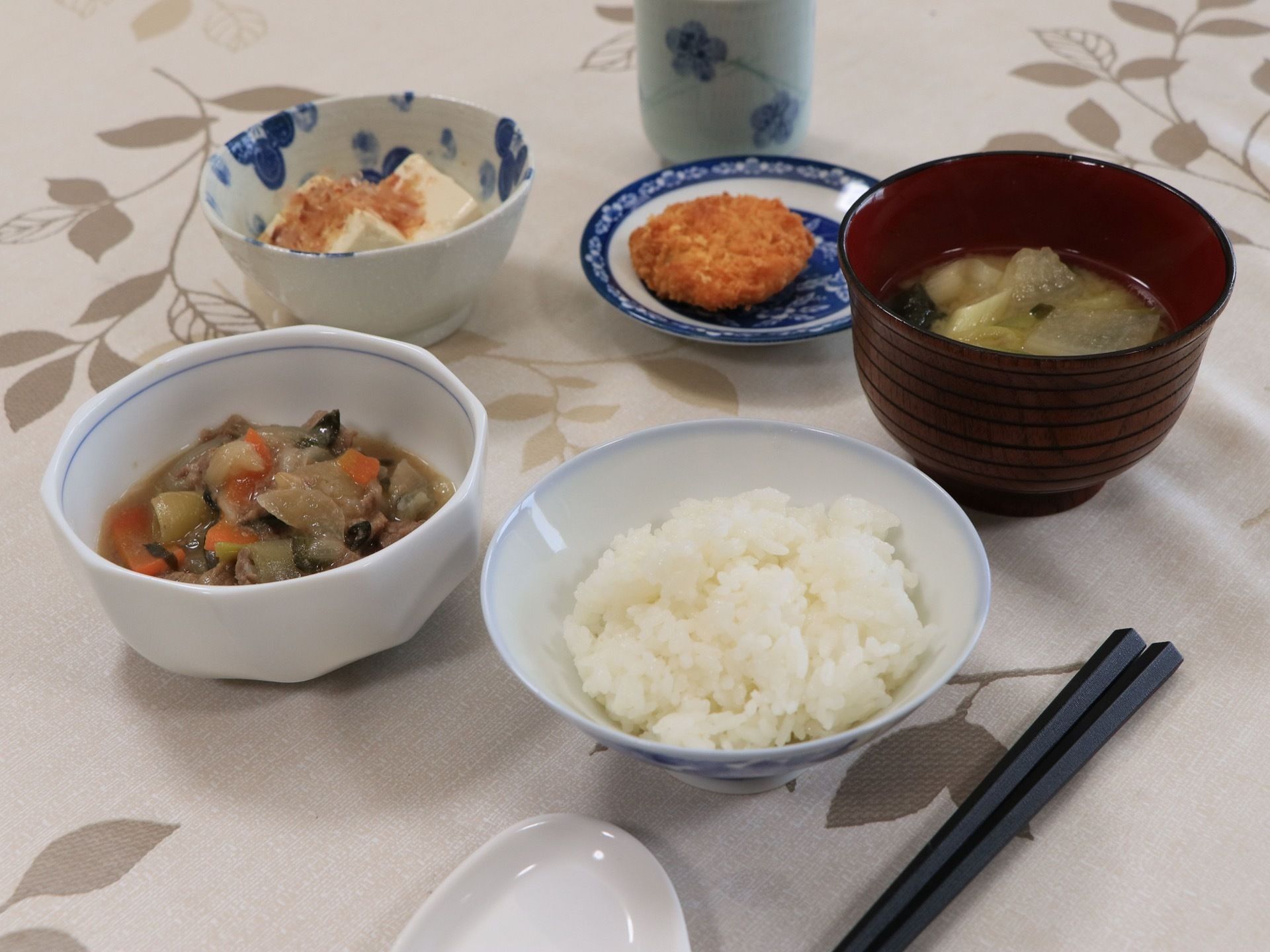 テーブルクロスの上に食事が配膳されている。メニューはごはん、お味噌汁のほか、揚げ物、冷ややっこ、煮物である。