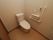 トイレには洋式便器が設置されている。壁側には操作ボタンと呼び出しボタン、トイレットペーパーフォルダー、手すりがつけられている。