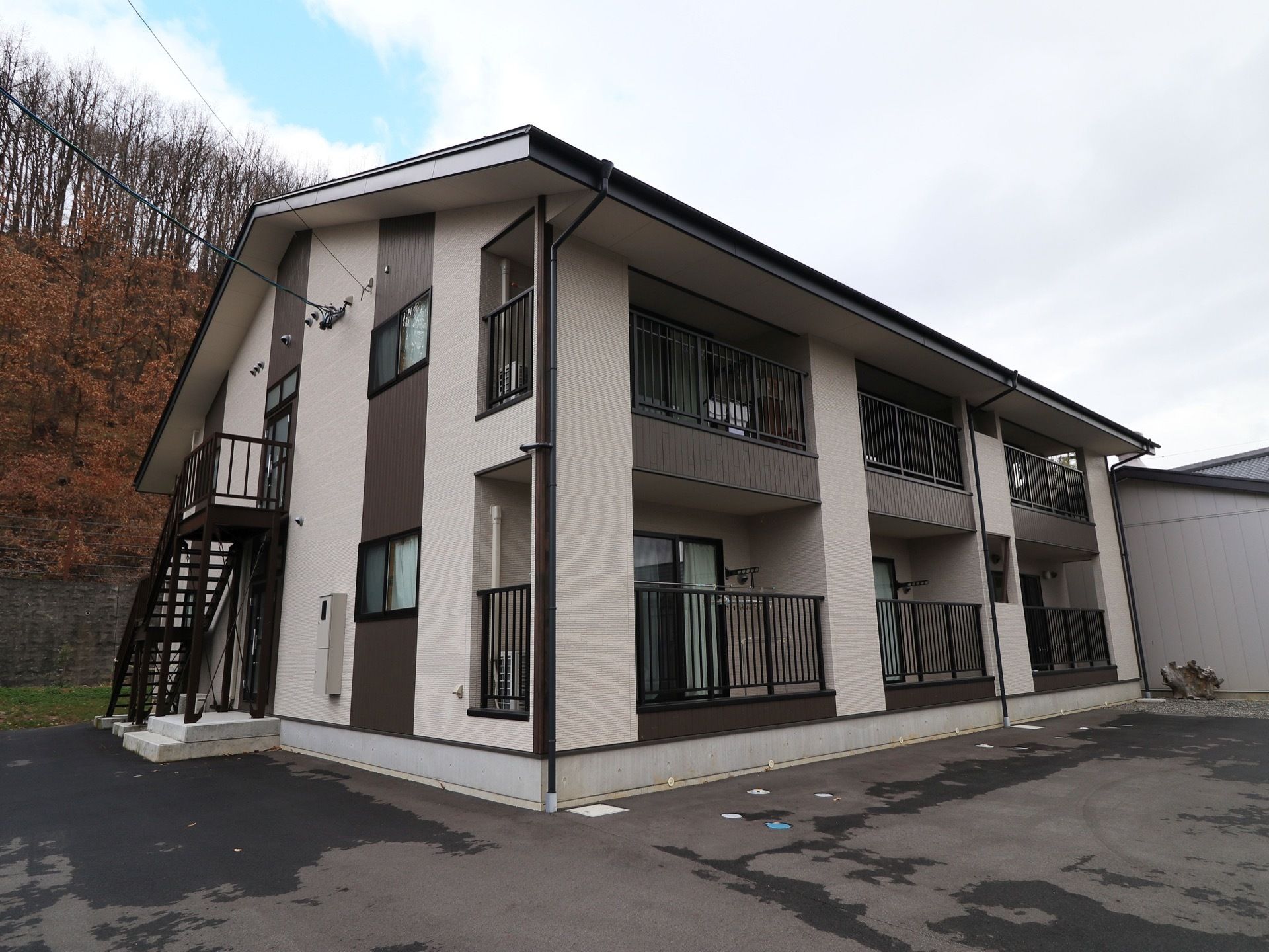 施設は2階建てで、外観は白色とダークブラウンの配色である。外階段があり、その後ろ側には木が生い茂っている。