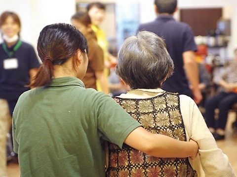 高齢者様を横からしっかり支えて歩く、施設の女性スタッフ