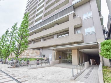 建物外観。高級感のあるつくりになっている。外には駐輪場とスロープがある。まっすぐ伸びた木が印象的だ。