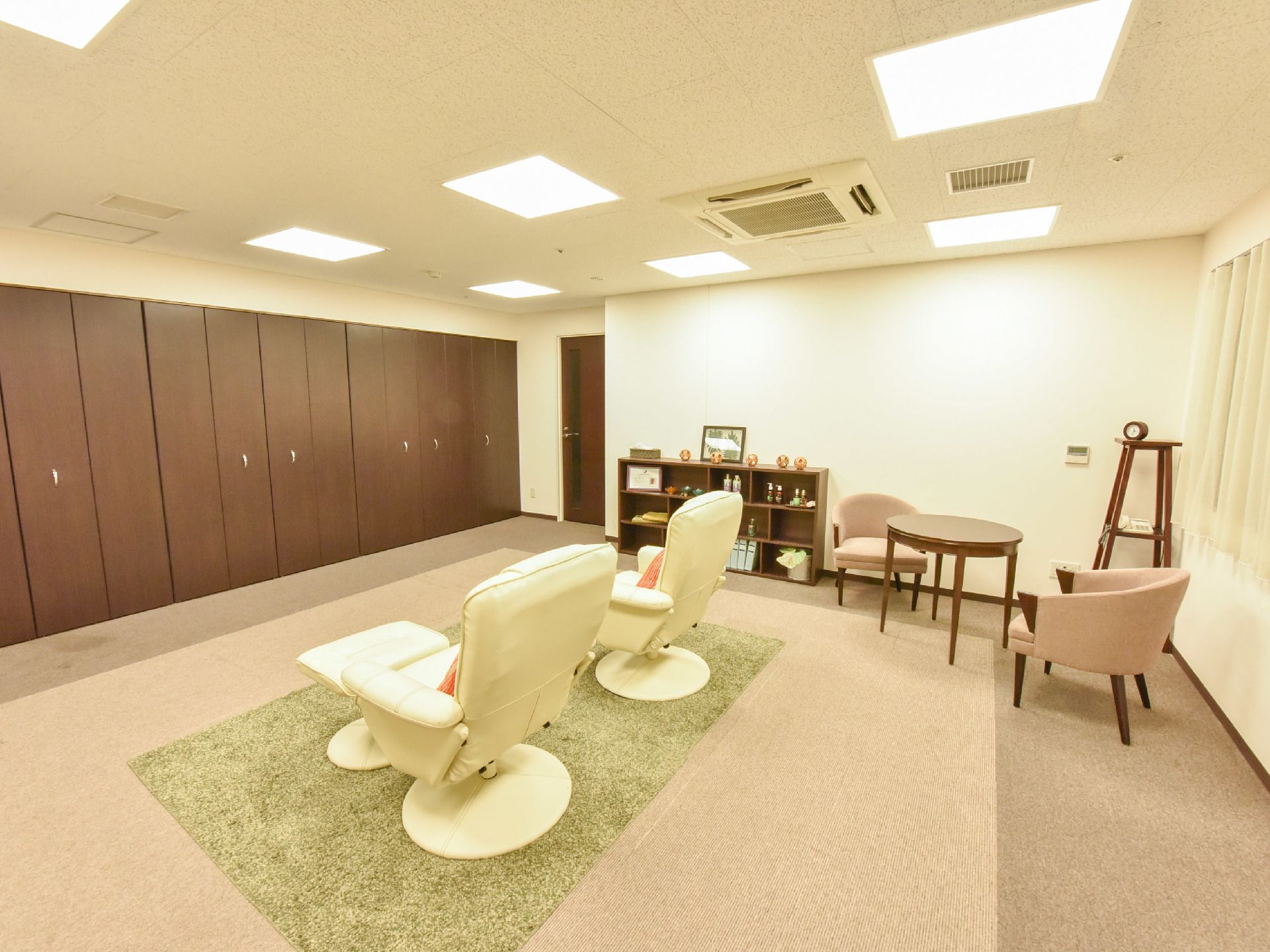 天井には四角のライトがいくつか灯っており左側の壁はウッド調の収納になっている。中央に白いソファが2脚並んでいる。