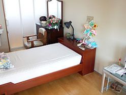 居室の壁に頭の方を向けてベッドを配置している。横側にドレッサーを置き、その上に花を飾っている。傍には椅子がある。