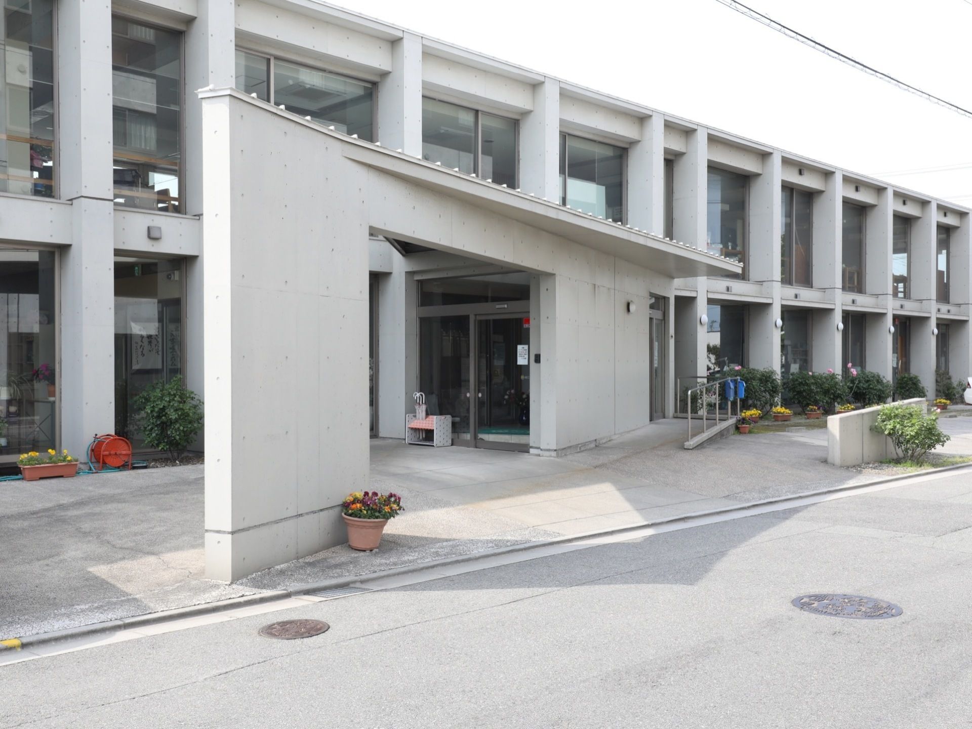 白い打ちっぱなしの外観がお洒落な、窓の多い二階建ての施設