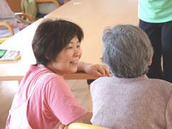 テーブルに着いた高齢者様に目線を合わせて話しかける施設スタッフ