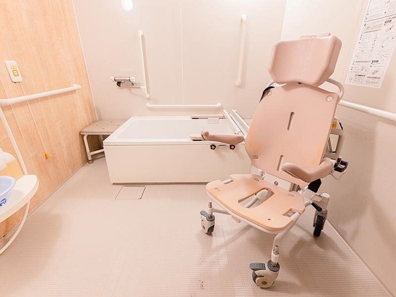 手すりや呼び出しボタンも設置された広い浴室。浴室用の車いすが置かれている。