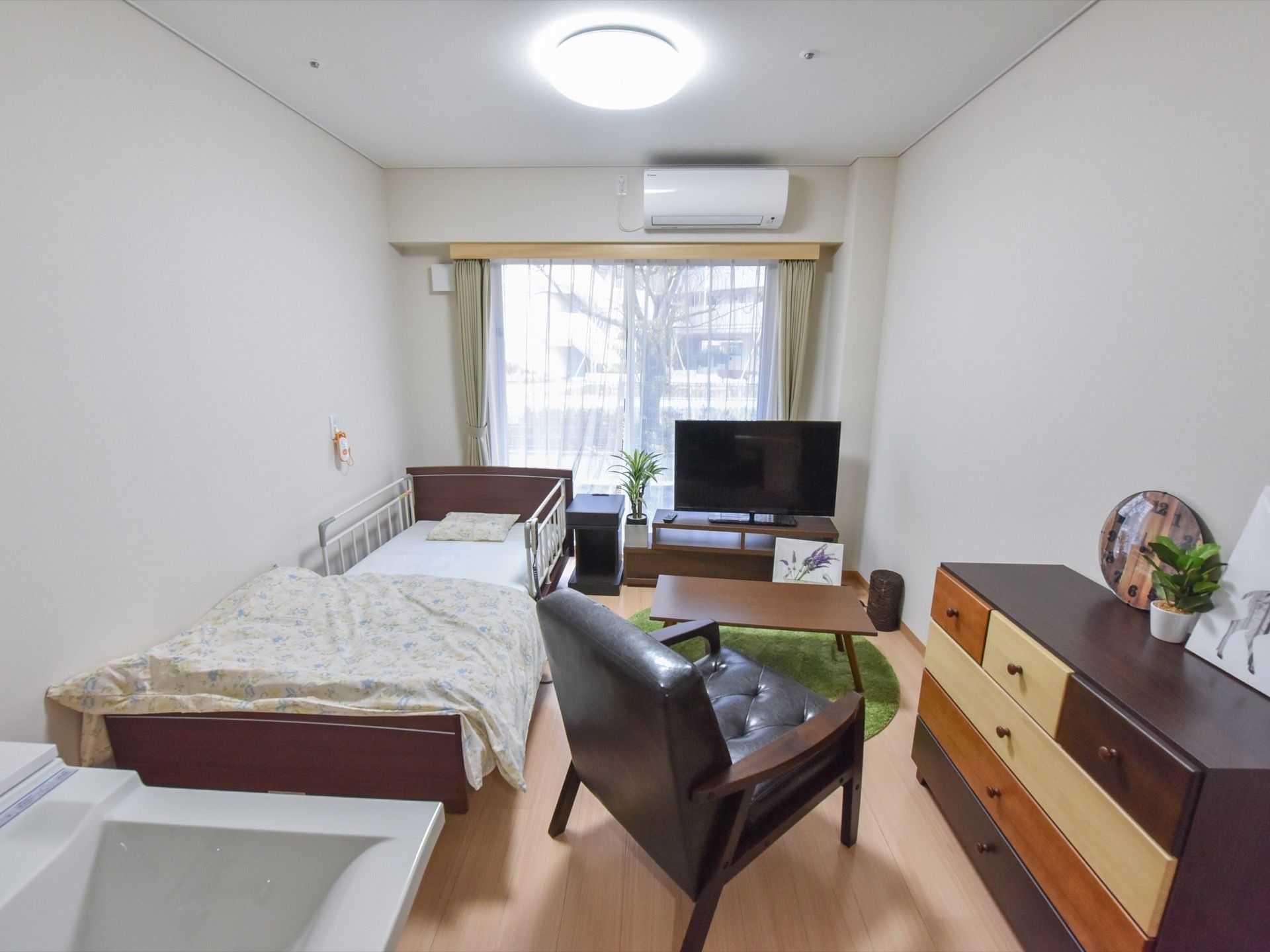 庭が眺められる窓に面した居室にはベッドの他、テレビや革張りの椅子、チェスト、テーブルなどが置かれている。