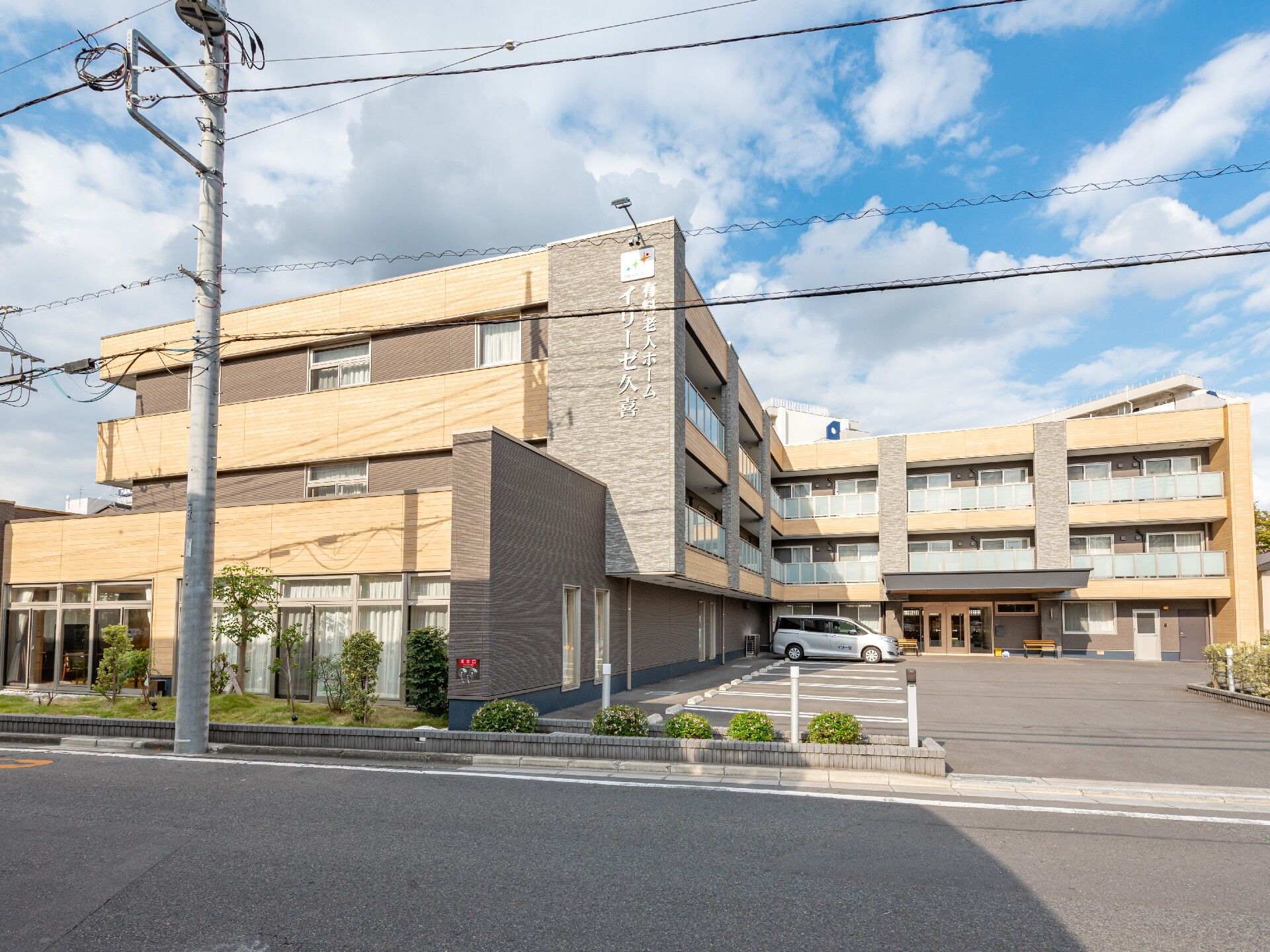 3階建ての施設の外観はブラウンと基調とした落ち着いた雰囲気になっている。建物の前には駐車場が設けられている。