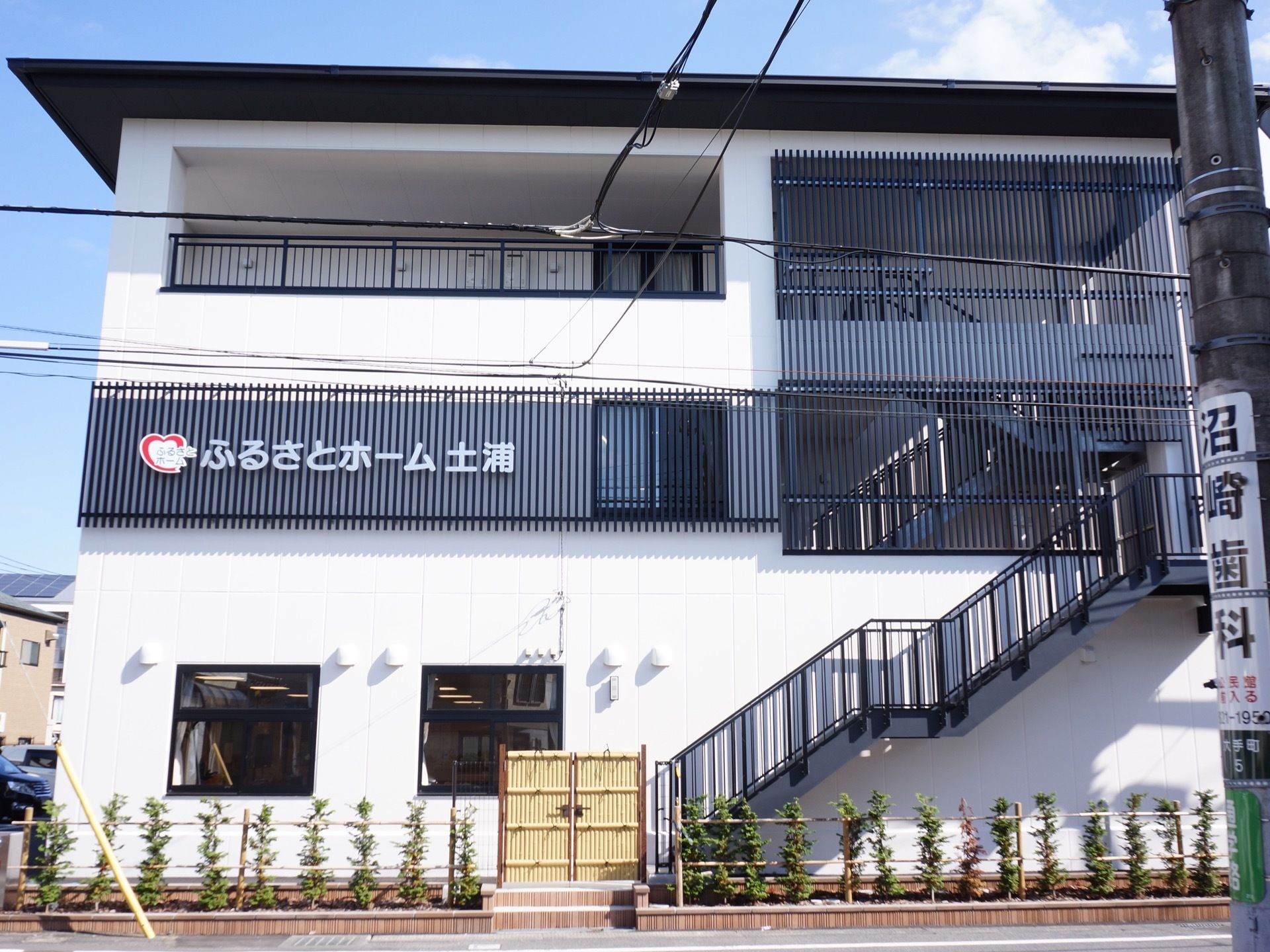 建物には、外階段があり、２階以上の階段には黒い格子が設置してある。道路側には目隠し用の木が植えてある。