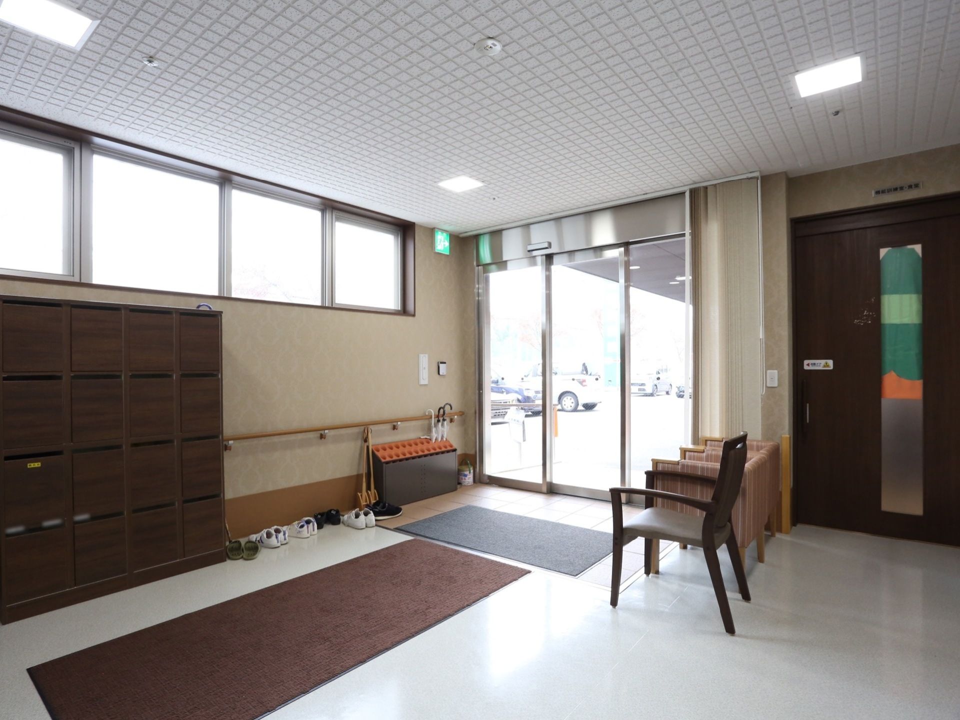 玄関内部に靴箱が設置されている。土間には足ふきマットや傘立てが置かれている。ソファと椅子が合わせて３つある。